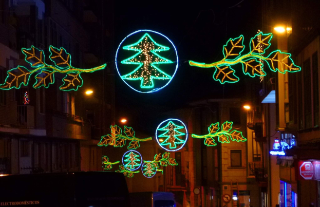Eine städtische Straße, geschmückt mit festlichen Weihnachtslichtern mit Blättern und anderen Verzierungen, mit Fahrzeugen, die die Straße entlangfahren und Gebäuden auf beiden Seiten.