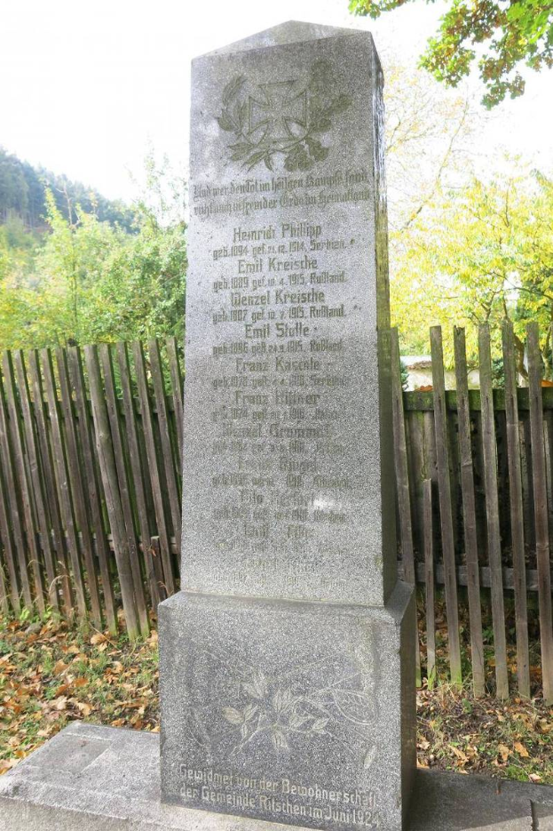 Ein Denkmal in einem Friedhof für deutsche Soldaten, die im Zweiten Weltkrieg starben, mit einem Holzzaun, Bäumen und einem klaren Himmel im Hintergrund.