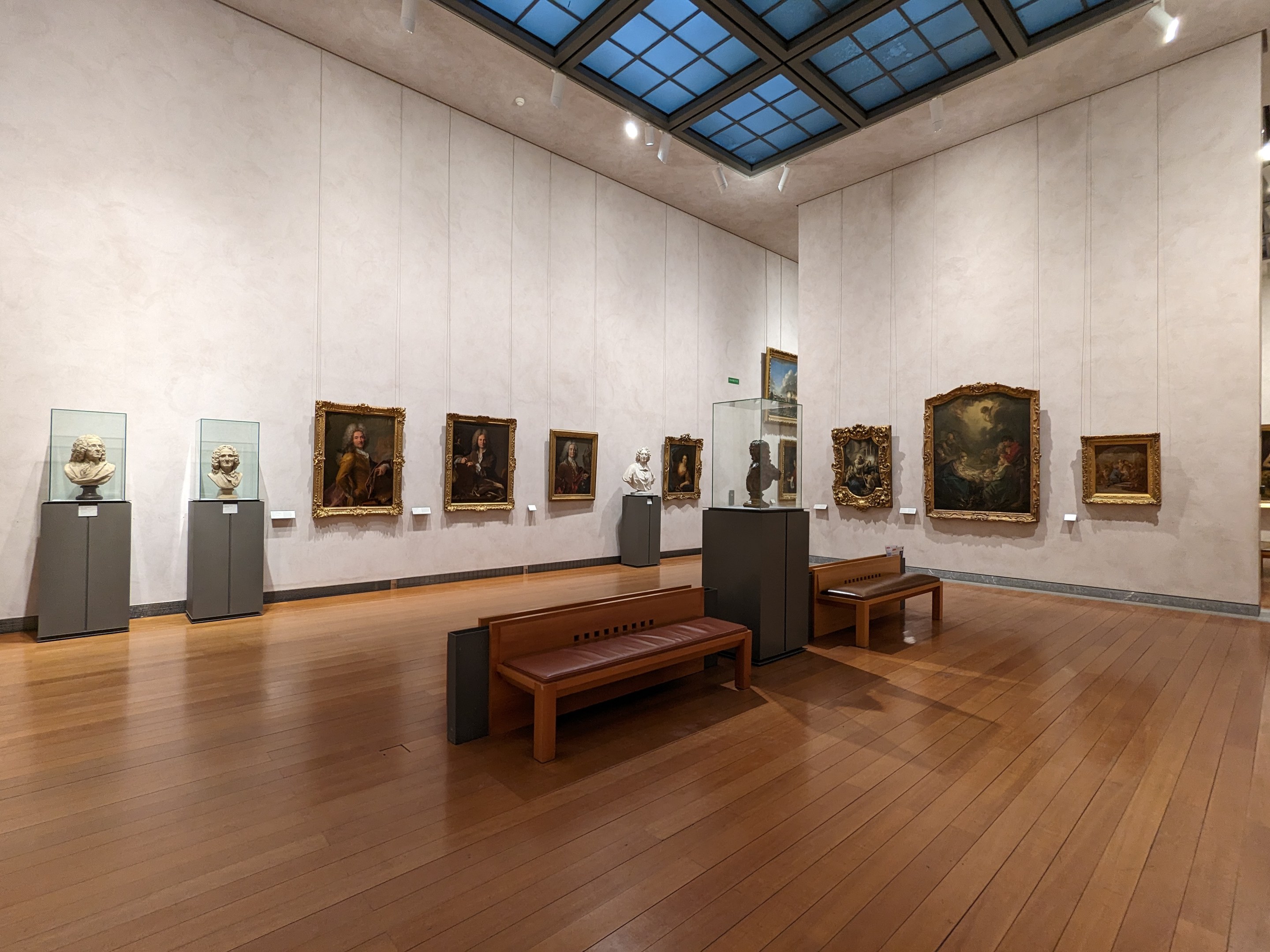 Eine große Galerie im Metropolitan Museum of Art mit zahlreichen Wandgemälden, freistehenden Skulpturen auf Sockeln, Sitzbänken und Deckenbeleuchtung.