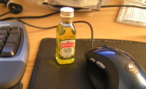 Ein Tisch mit verschiedenen Gegenständen, darunter Kabel, eine Maus, eine Tastatur, eine Scheibe, Notizen, eine Flasche mit Flüssigkeit und eine Mausmatte.