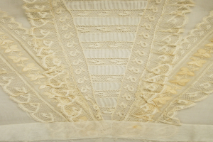 Nahaufnahme eines weißen Kleides mit zarter, detaillierter Spitzenverzierung auf einem leichten, luftigen Stoff.