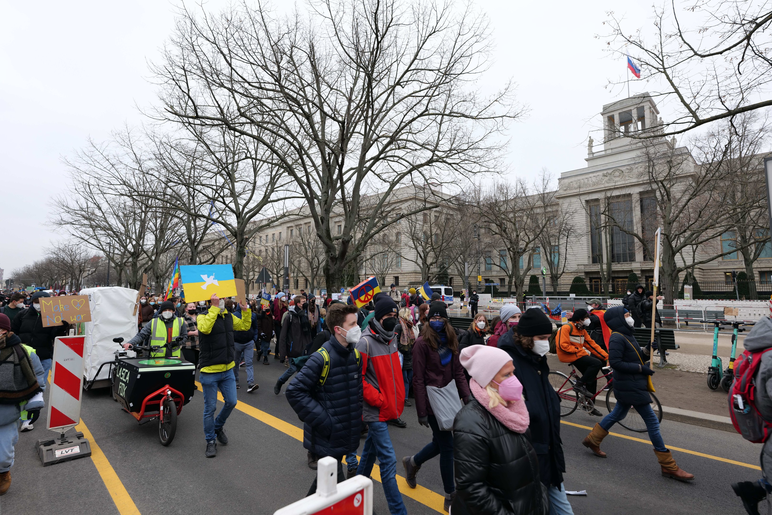 Eine große Gruppe von Menschen marschiert auf einer Demonstration in Washington, D.C. am 21. Januar 2020, einige halten Schilder und Banner, andere fahren Fahrräder, mit Bäumen und einem klaren blauen Himmel im Hintergrund.