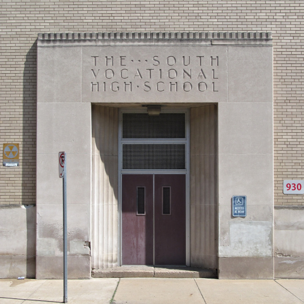 Das Südliche Berufsbildungszentrum mit einer Tür, Schilder an der Wand und einem Weg, der zur Eingangstür führt.