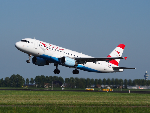 Airbus A320-200 der Austrian Airlines beim Start am Frankfurter Flughafen, mit grünem Gras, Bäumen, Gebäuden und einer Kontrollturm im Hintergrund.