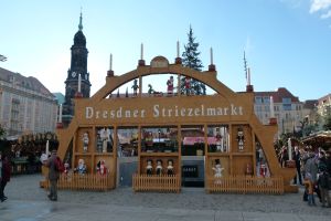 Ein lebendiger Weihnachtsmarkt in Dresden, Deutschland, mit Menschen, die herumlaufen, einem Bogen mit Text, Tänern, Gebäuden mit Fenstern und einem bewölktem Himmel.