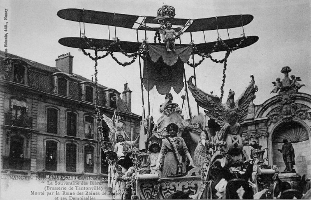 Ein Schwarz-Weiß-Foto eines Paradewagens, der mit Statuen und einem Flugzeug geschmückt ist und eine Gruppe von Menschen trägt, mit einem Gebäude und Himmel im Hintergrund und Text unten, der darauf hinweist, dass es ein Foto des Pariser Karnevals ist.