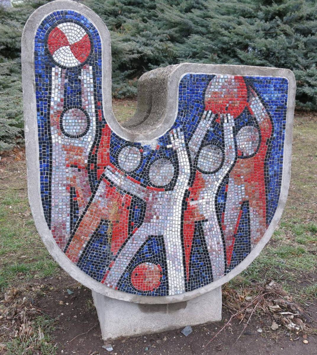 Eine Mosaikbank in einem Park, umgeben von Bäumen, mit einem klaren blauen Himmel, aus farbigen Fliesen in einem einzigartigen Design.