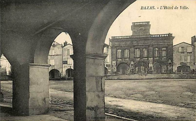 Schwarz-weiß-Foto einer Stadtstraße mit Gebäuden, Bögen und einer Eisenbahnschiene, beschriftet mit "bazas - l'hotel de ville" oben und unten.