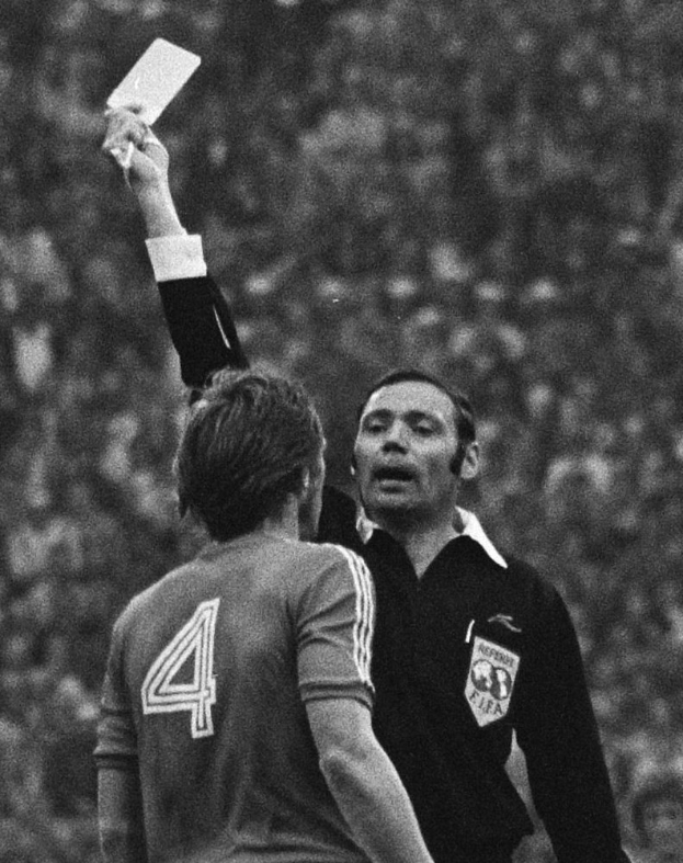 Ein Schiedsrichter in einem Schwarz-Weiß-Foto hält eine weiße Karte einem Fußballspieler entgegen, mit einem unscharfen Hintergrund.