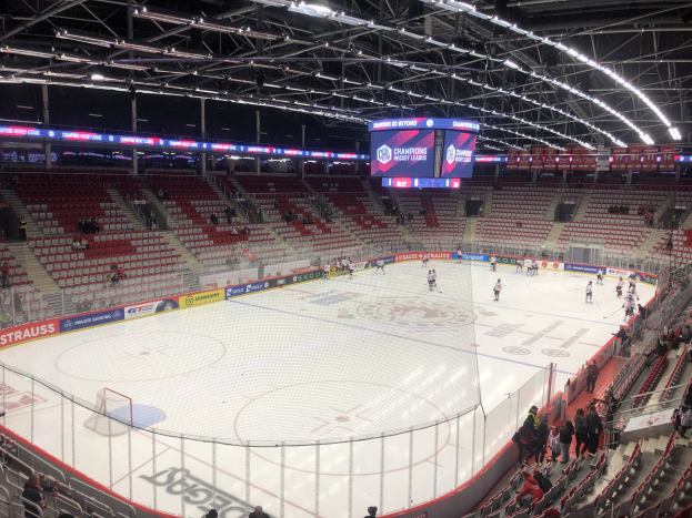 Eishockeyspiel in einer großen Arena mit Zuschauern, ein Rink umgeben von einem Zaun, ein Display mit der Aufschrift "St. Louis Blues vs Detroit Red Wings" und Deckenbeleuchtung.