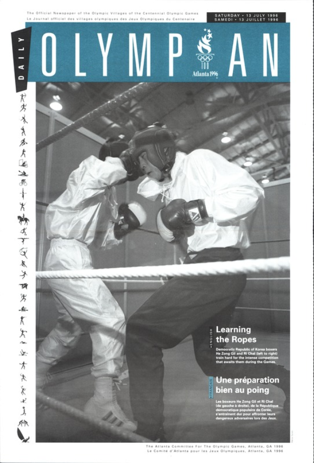 Zwei Boxer im Ring, mit Helmen und Handschuhen, Seilen und Lichtern und "Olympian Magazine"-Text oben und unten.
