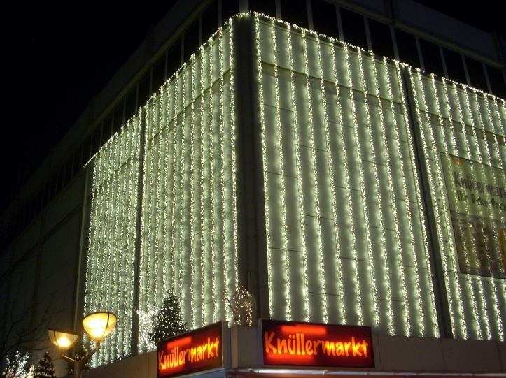 Ein Gebäude in Berlin, Deutschland, geschmückt mit Weihnachtslichtern, umgeben von Bäumen, Laternenmasten und Texttafeln, mit dem Himmel im Hintergrund.