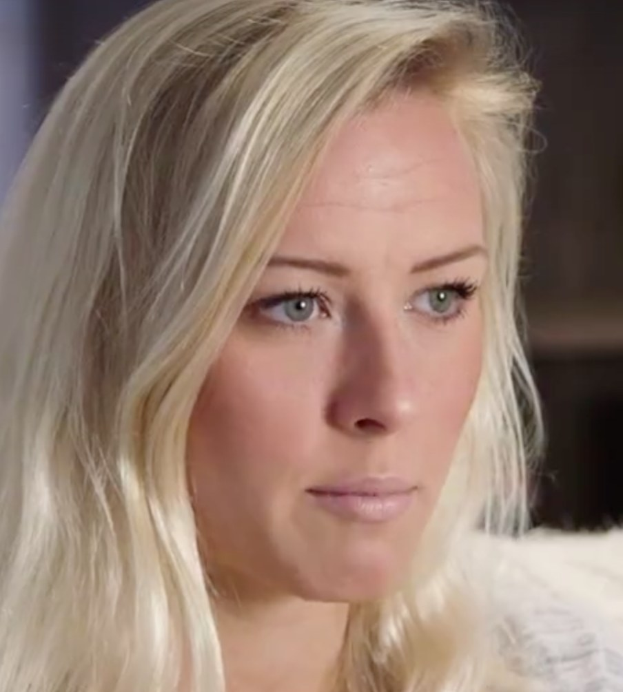 Blonde Frau mit blauen Augen im Vordergrund, unscharfer Hintergrund, wirkt beunruhigt.