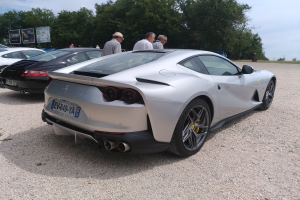 Roter Ferrari 812 Superfast auf dem Goodwood Festival of Speed umgeben von Zuschauern mit Mützen, Bäumen, Informationsschildern und einem bewölkten Himmel im Hintergrund.