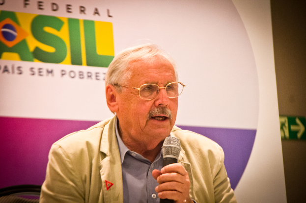 Eine Person, die in ein Mikrofon spricht und im Hintergrund ein Banner mit dem Wort 'Bundes' trägt.