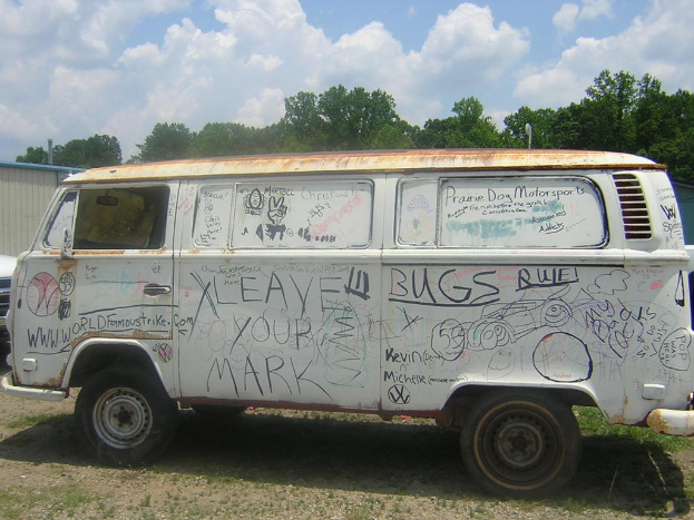 Ein demolierter Van mit Gemälden und Zitaten darauf, der vor einer Baumgruppe geparkt ist.