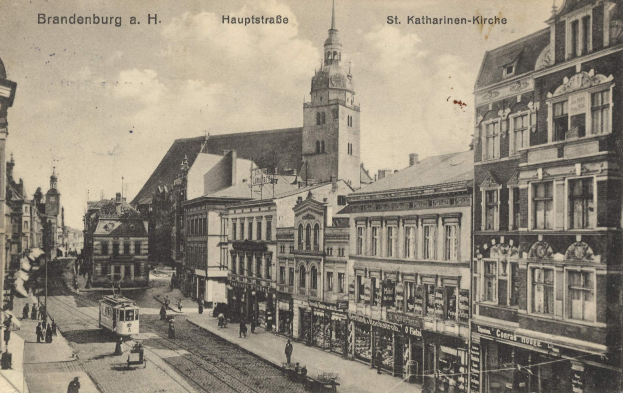 Ein altes Schwarz-Weiß-Foto einer Straßenansicht in Brandenburg, Deutschland, mit einer Tram auf Schienen, Passanten, Gebäuden mit Fenstern und einem bewölkten Himmel, mit Text oben und unten im Bild.
