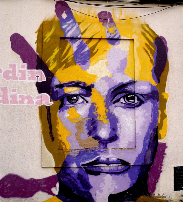 Ein leuchtendes, farbenfrohes Wandgemälde eines Frauenkopfs auf einem Berliner Gebäude, das detaillierte Züge und großen Text aufweist.