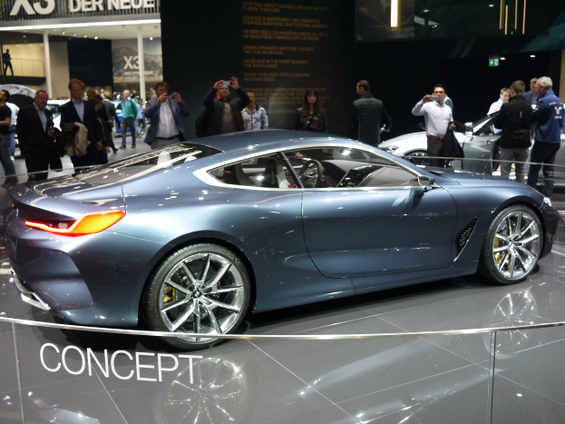 Ein BMW 8er-Konzeptfahrzeug mit glänzender schwarzer Lackierung und Chromakzenten wird auf der Frankfurter Motorshow präsentiert, umgeben von Menschen, die Fotos machen, mit beleuchtetem Hintergrund und einem Textschild.