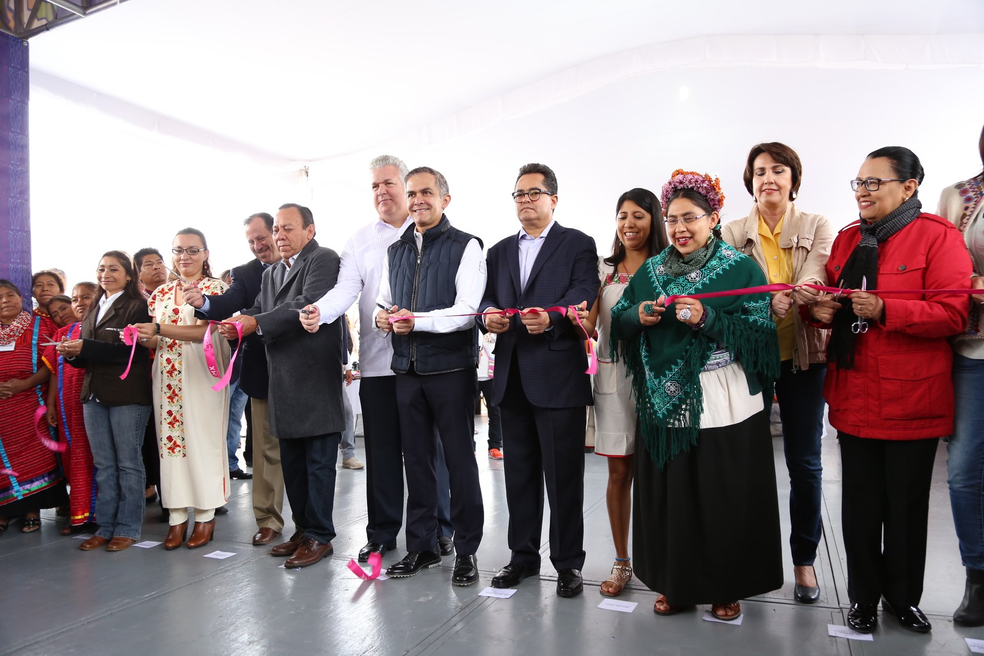 Eine Gruppe von Menschen, die eine Schnur durchschneiden, mit einem strahlenden Lächeln und einer Schere in der Hand, mit Papieren auf dem Boden und einem weißen Tuch im Hintergrund.