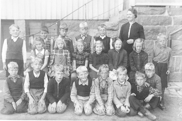 Schwarz-weiß-Foto einer Gruppe von Kindern, die vor einem Gebäude mit Treppe und Geländer posieren, beschriftet mit "1930er Schulkinder."