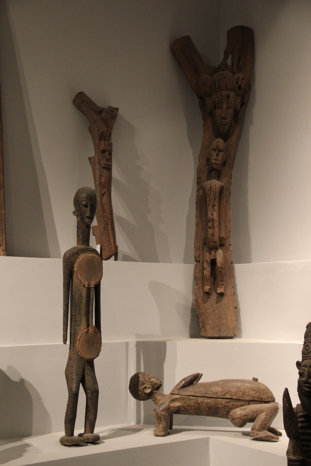 Eine Gruppe von Holzskulpturen, die auf einer weißen Oberfläche in einem Museum ausgestellt ist, mit einer Wand im Hintergrund.