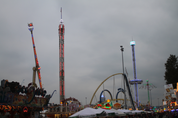 Eine Menschenmenge versammelt sich um einen hell erleuchteten Faschingsumzug in der Nacht, mit beleuchteten Fahrgeschäften, Pfählen und Bäumen unter einem bewölkten Himmel.