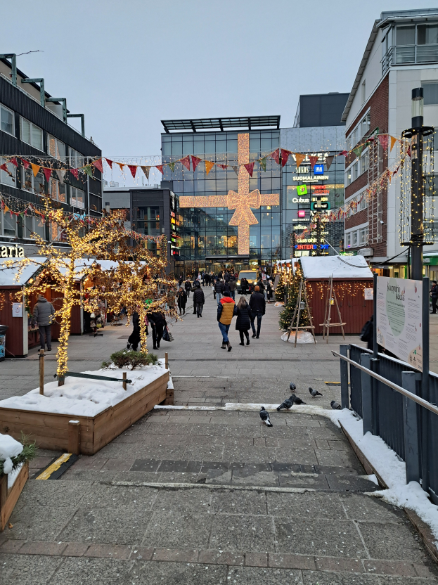 Eine belebte Stadtstraße mit Menschen, die auf einem schneebedeckten Gehweg laufen, flankiert von Gebäuden mit geschmückten Weihnachtsbäumen und Vögeln im Hintergrund.