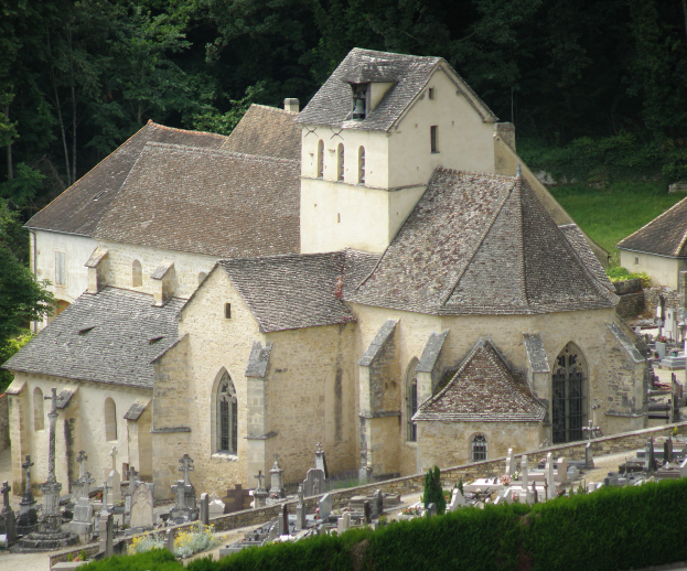 Eine alte Kirche mit einem Friedhof voller Grabsteine vorne, umgeben von Häusern, Bäumen, Pflanzen und Gras, die eine friedliche und friedliche Atmosphäre schaffen.