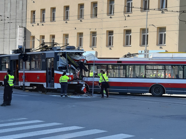Eine rote und weiße Straßenbahn, die in einen Unfall auf der Straße verwickelt ist, mit ein paar Menschen in der Nähe und einem Gebäude im Hintergrund.