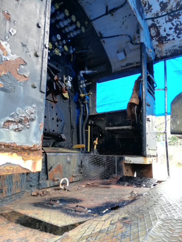 Das Innere eines verrosteten, baufälligen Lastwagens mit sichtbaren Spuren von Abnutzung, vor einem Hintergrund aus Bäumen und einem klaren blauen Himmel.