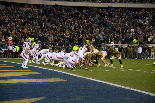 Fußballspieler in Sportkleidung und Helmen auf dem Boden während eines Spiels in einem Stadion mit Zuschauern und Tafeln im Hintergrund.