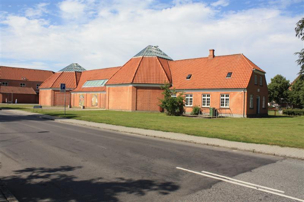 Ein großes Ziegelgebäude mit rotem Dach, umgeben von Grün und Schildern, das an der Seite einer Straße steht, unter einem bewölkten Himmel, das die neue Schule in den Niederlanden darstellt.