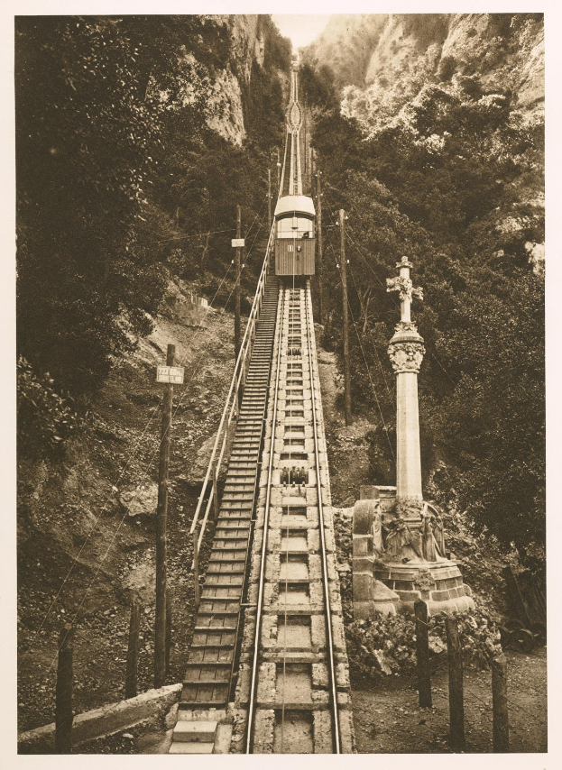 Schwarzes und weißes Foto eines Zuges, der eine steile Steigung hinauffährt, mit einem Pfahl auf der rechten Seite und Bäumen im Hintergrund; Text unten.