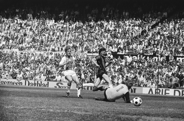 Ein Schwarz-Weiß-Bild einer Gruppe von Männern, die auf einem Feld Fußball spielen, mit Zuschauern im Hintergrund und einem Banner mit der Aufschrift "Bundesliga 1978-79 Ajax 1-1 Hannover 96."