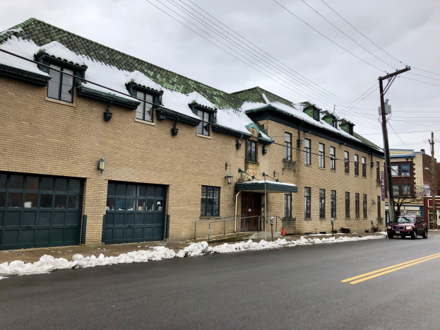 Großes Ziegelgebäude mit grüner Dachfläche an einer Straßenkreuzung, umgeben von Fahrzeugen, Schnee, Strommasten, Bäumen und einem bewölkten Himmel, identifiziert als die ehemalige Feuerwache St. Louis.