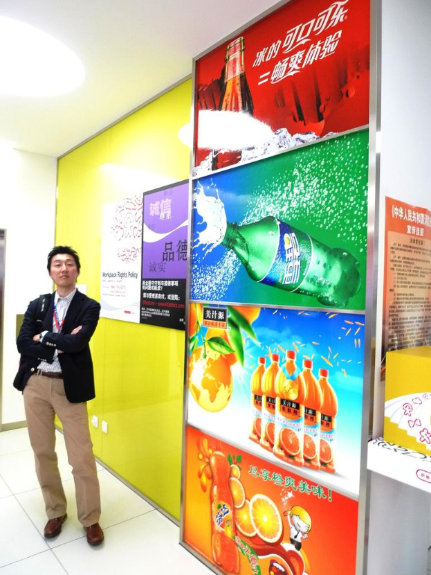 Ein Mann im Blazer steht vor einer Wand mit Softdrinkwerbung.