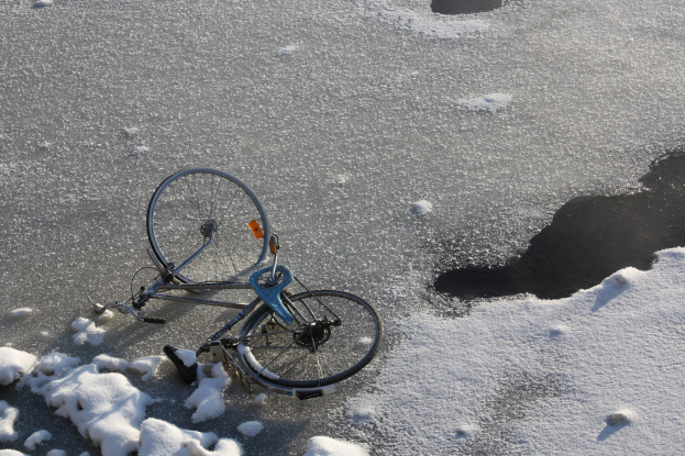 Ein Fahrrad im Schnee neben einer Pfütze Wasser liegend, mit einer Schneedecke drumherum.