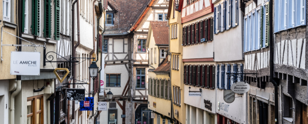 Enge Straße in Colmar, Elsass, Frankreich, gesäumt von Gebäuden mit Fenstern, Namensschildern, Lichtern und Röhren, über einer Straße.