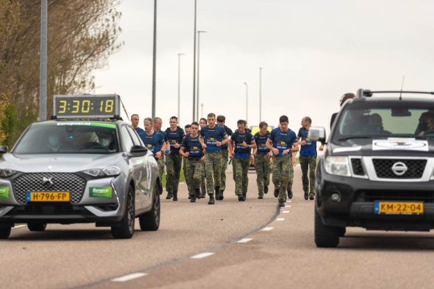 Gruppe von Menschen, die auf einer Straße neben Autos mit Bäumen auf der linken Seite und Masten im Hintergrund gehen, während einer Europäischen Cross-Country-Challenge.
