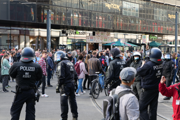 Eine Gruppe von Polizisten steht vor einer Menschenmenge auf der Straße, einige halten Fahrräder, mit Gebäuden, Namensschildern, Laternen und Regenschirmen im Hintergrund.
