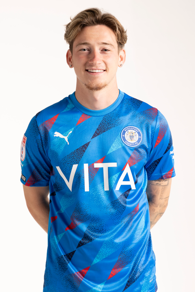 Ein junger Mann in einem blauen Auswärtstrikot von Leicester City aus der Saison 2019/20, der gegen einen weißen Hintergrund steht und lächelt.