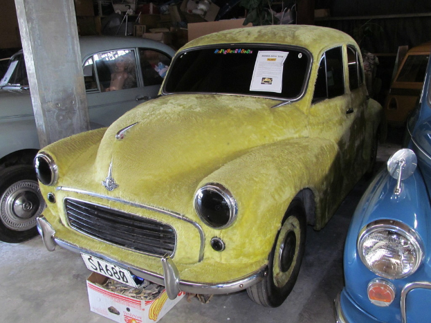Eine Reihe von Oldtimern, die vor einer Wand mit verschiedenen Accessoires geparkt sind, mit einer Säule auf der linken Seite.
