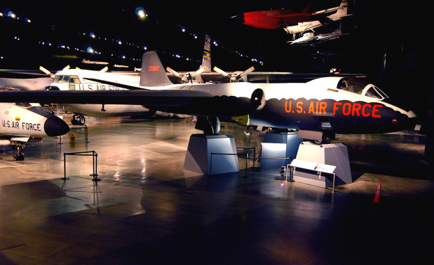 Eine Gruppe von Kampfflugzeugen in einem Museum ausgestellt, umgeben von St├Ąnden, Verkehrskegeln und anderen Gegenst├Ąnden auf dem Boden, mit dunklem Hintergrund und fokussiertem Licht.