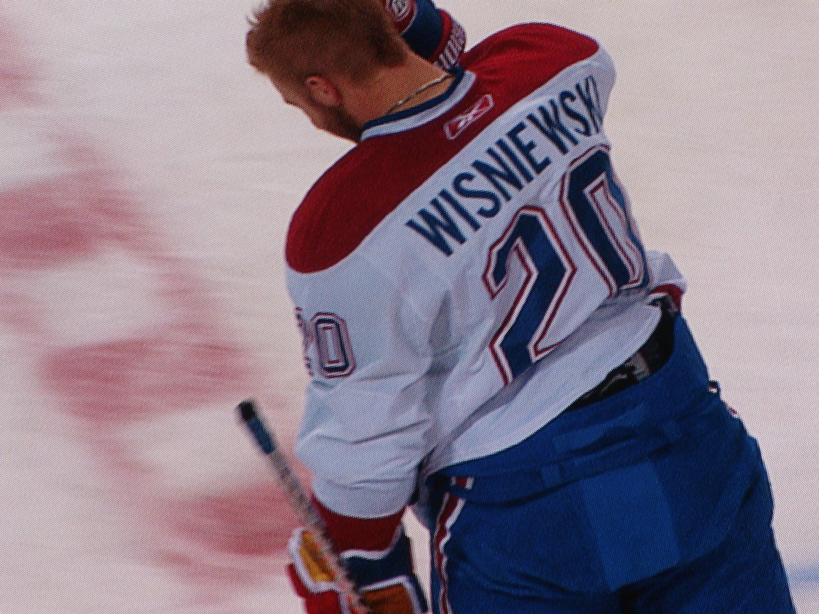 Ein Hockey-Spieler in einem "Wisniewski"-Trikot steht auf dem Eis, hält einen Hockey-Schläger und hat einen konzentrierten und entschlossenen Gesichtsausdruck.