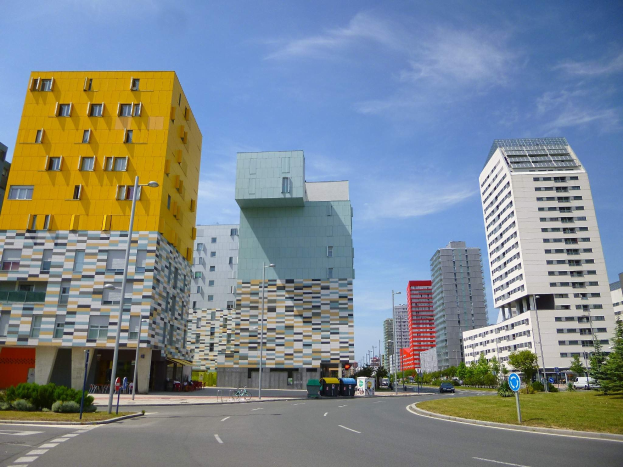 Eine Stadtstraße mit hohen Gebäuden im Hintergrund, Straßenlaternen, Autos, Informationsschildern, Büschen, Bäumen und einer bewölkten Himmel, mit Gebäuden der Universität Rotterdam mit einzigartiger Architektur.