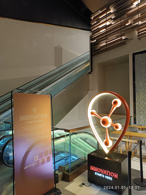 Großes Schild in der Mitte eines Gebäudes mit einer Treppe im Hintergrund, flankiert von Tischen und Stühlen auf der rechten Seite und einer Tafel mit der Aufschrift "Innovation beginnt hier" auf der linken Seite, die auf die HSTP20 Expo hinweist.
