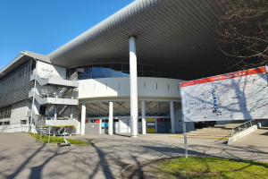 Großes Gebäude mit vielen Fenstern, Säulen und Treppen, das als Eingang zum Olympiastadion in London dient, mit einem Wagen, Gras, einer Straße, Bäumen und Himmel im Hintergrund.
