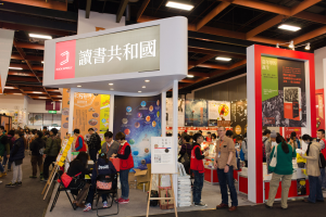 Eine große Gruppe von Menschen an einem Messestand mit Stühlen, Texttafeln, Bannern und Deckenbeleuchtung, die "Book Republic Hong Kong Book Fair" anzeigt.