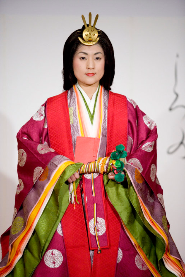 Eine Frau in einem traditionellen japanischen Kimono, mit einem leuchtend roten und grünen Kleid mit aufwändigen Mustern, steht selbstbewusst auf einem Laufsteg, ihr Haar zu einem ordentlichen Knoten gebunden.